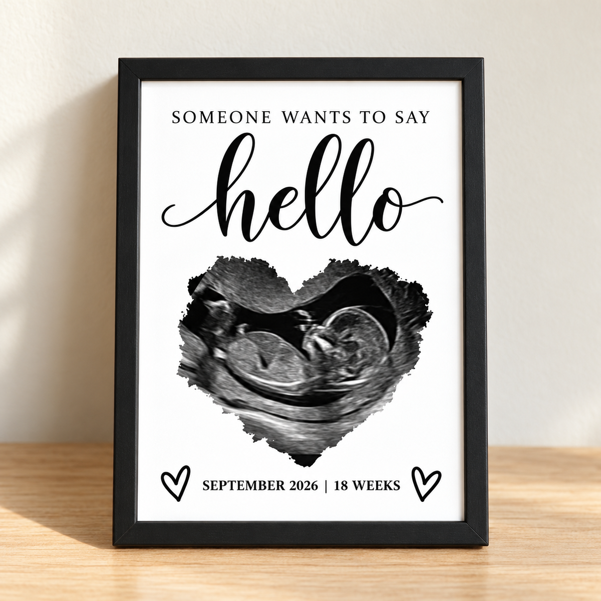 Someone wants to say hello personalized 5x7 ultrasound print in a black frame on a light wood table; sample personalization